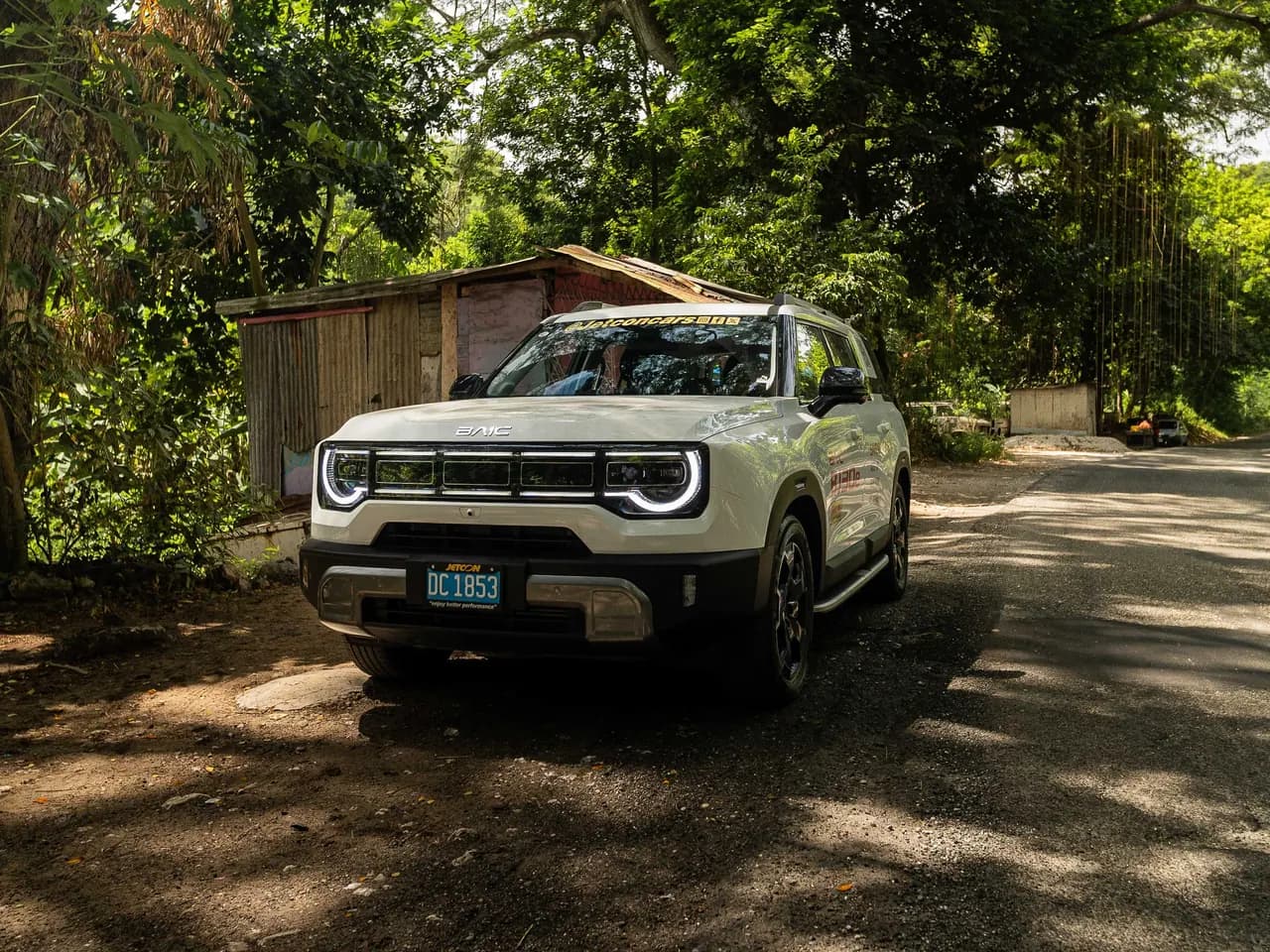 White BAIC BJ30e parked under trees beside a zinc-roofed roadside shop, front view