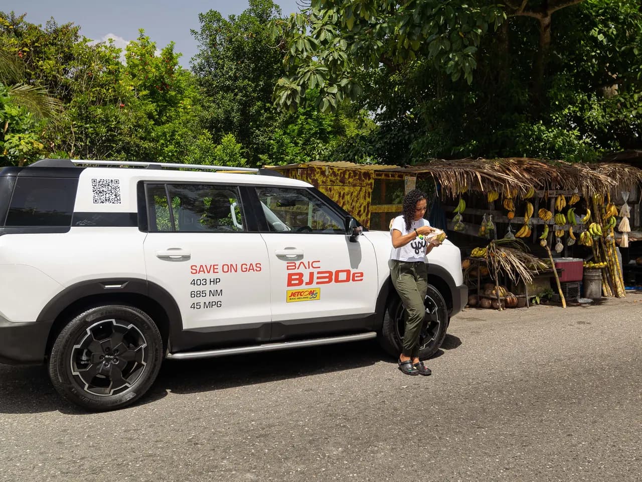 White BAIC BJ30e in profile beside a roadside fruit stall hung with bananas and sugar cane