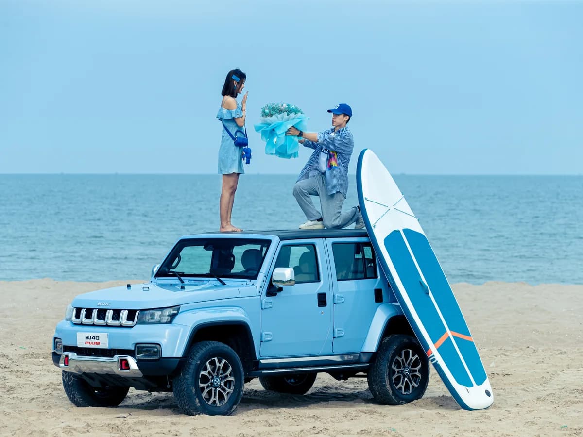 Light blue BAIC BJ40 Plus on a beach with a paddleboard on the roof
