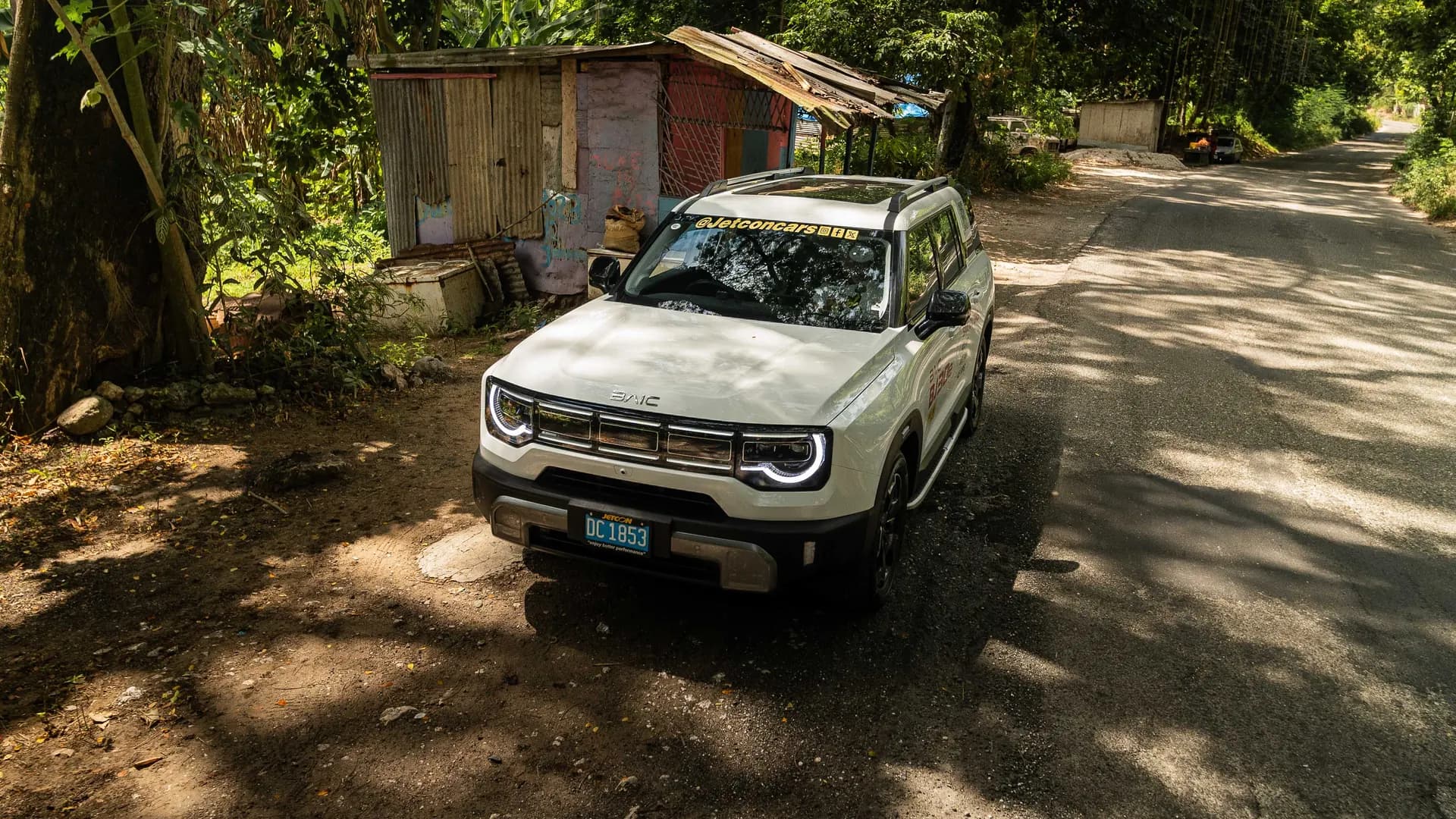 White BAIC BJ30e on a shaded Jamaican country road, seen from a high front three-quarter angle